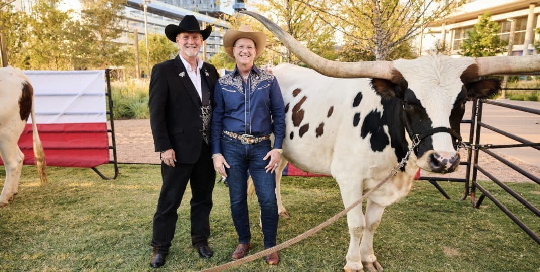 Two people in western wear beside a Texas longhorn at a park celebration
